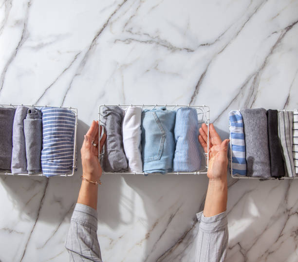 Neatly folded clothes and pyjamas in the metal mesh organizer basket on white marble table. Marie Kondo style of garments declutter and sorting concept. Housewife using Konmari method of tidying up.